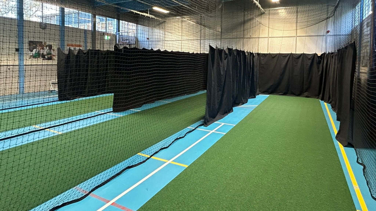 Indoor cricket training facility featuring Durant Cricket Roll-Down surface with netting and protective curtains.