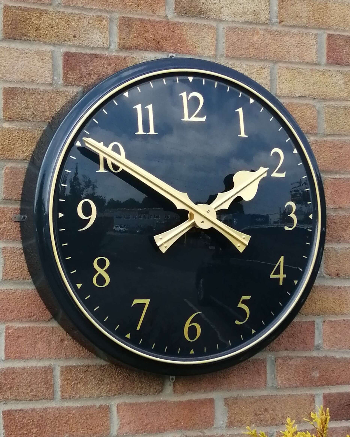 Cricket Pavilion Clocks featuring a traditional design with black dial and gold hands mounted on a brick wall.