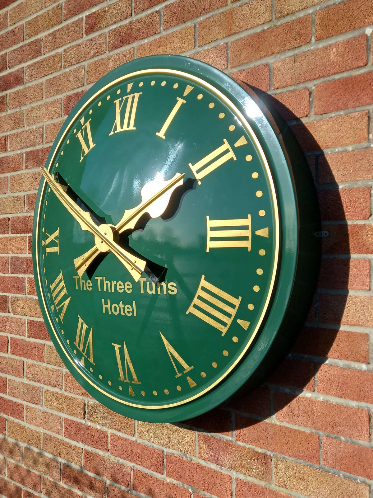 Cricket Pavilion Clocks featuring an elegant green dial with gold numerals and hands mounted on a brick wall.