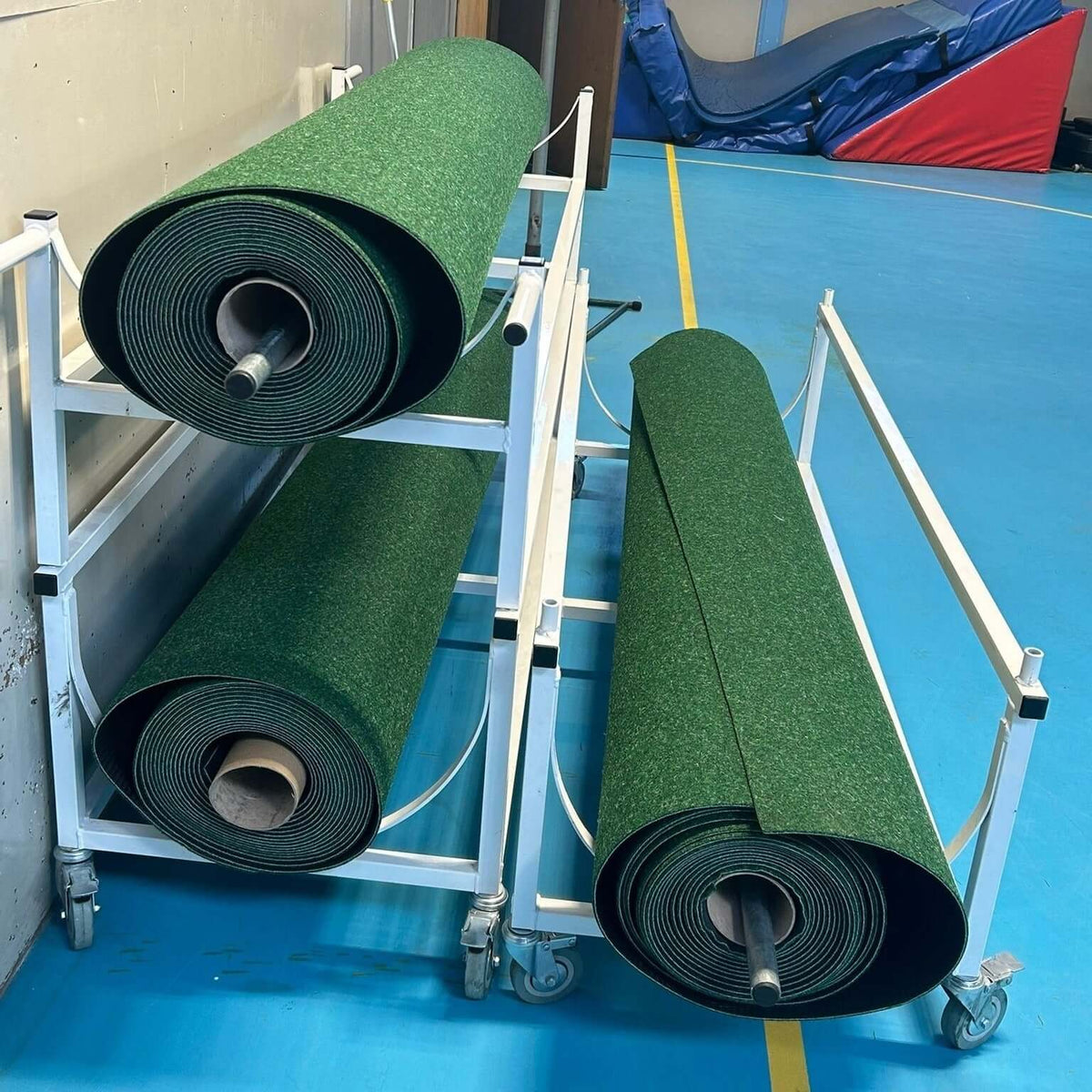 Durant Cricket Roll-Down rolls displayed on a trolley in a sports facility, showcasing the green surface for indoor use.