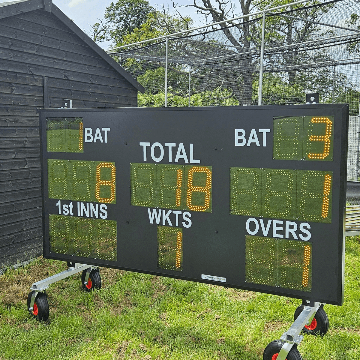 Scoreboard Trolley displaying cricket score with total, wickets, and overs on a grass field backdrop.