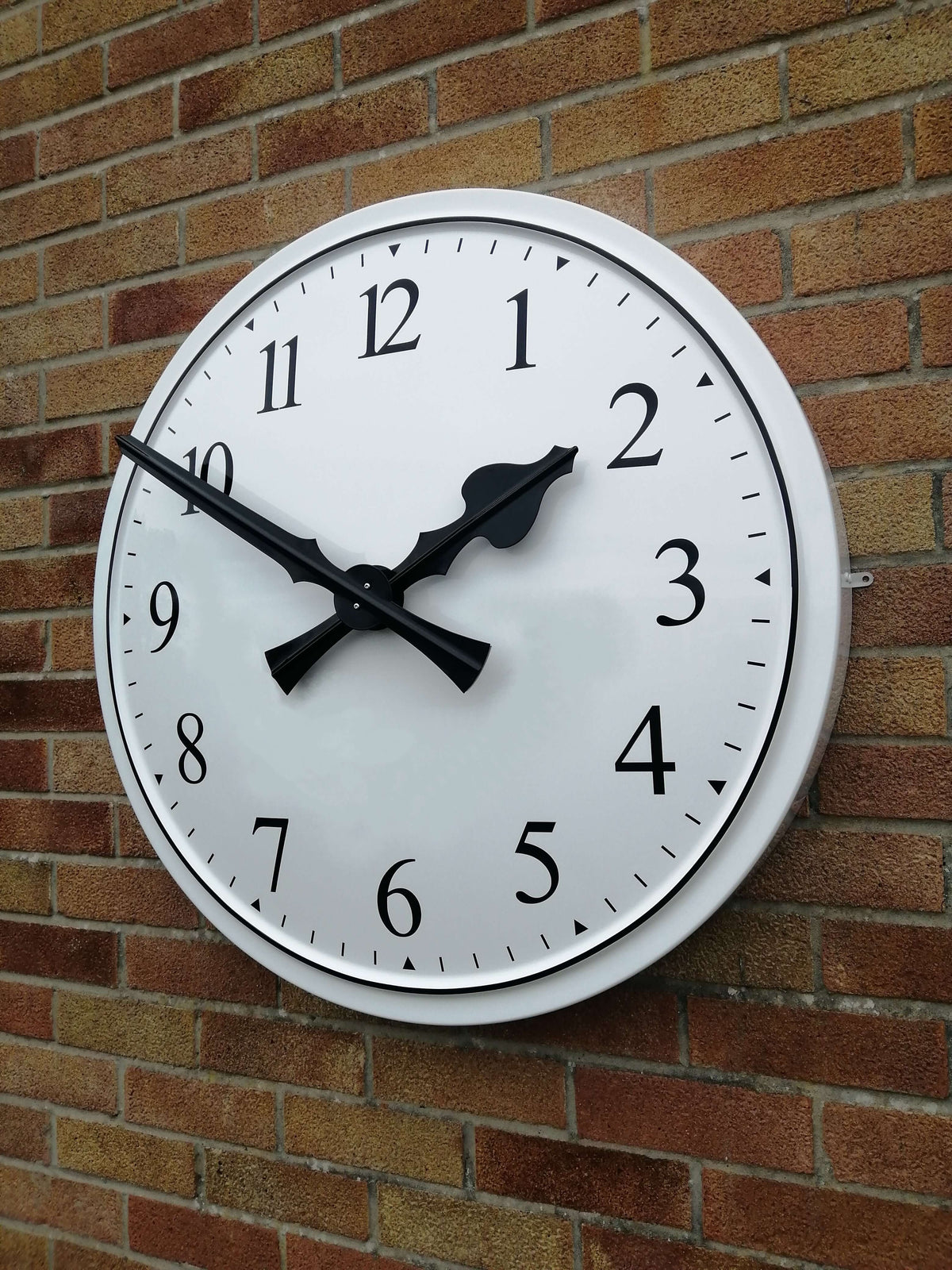 Cricket Pavilion Clocks mounted on a brick wall showing traditional dial design and black numerals.