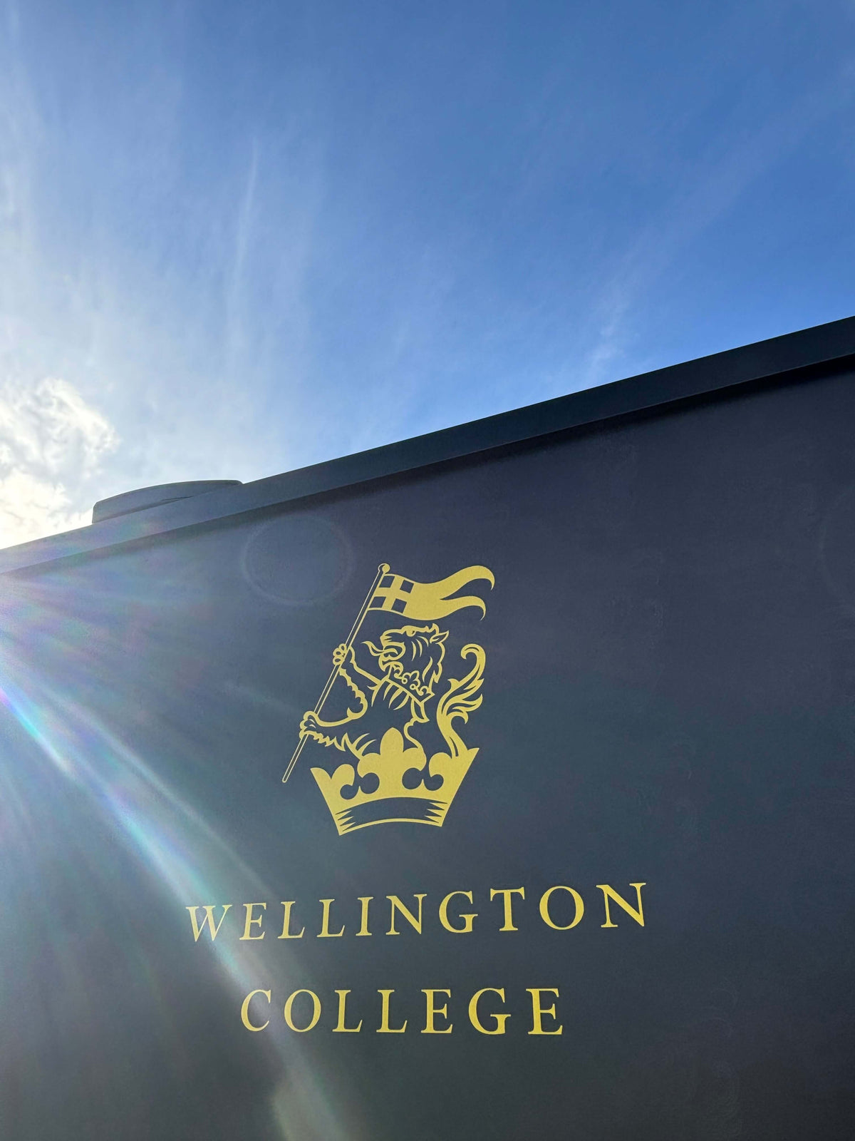 Wellington College emblem with a lion and crown, under a clear blue sky.